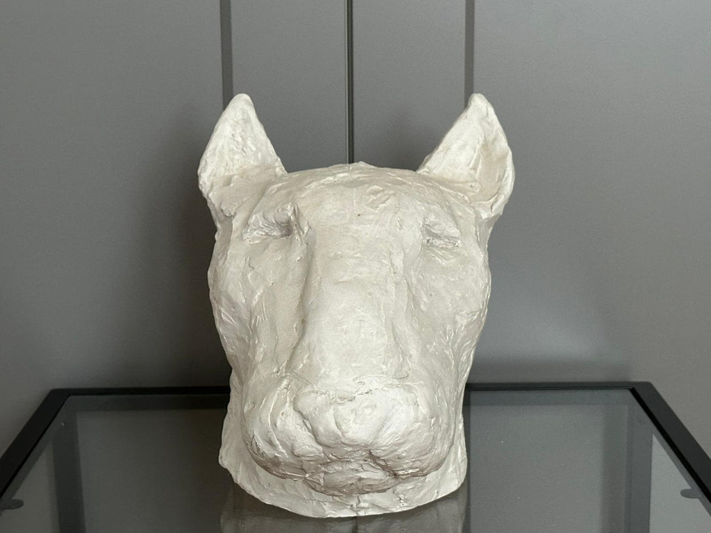 White gypsum sculpture of a dog's head on a dark surface with a gray background